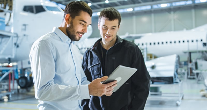 Two men studying tablet in aircraft hangar