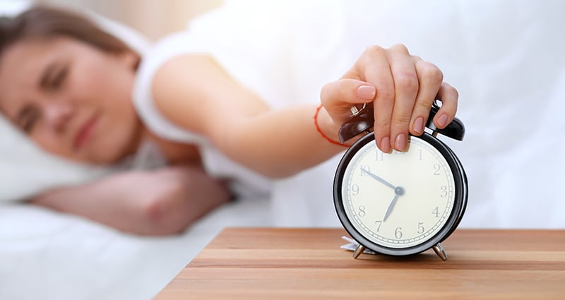 Woman hitting snooze on her alarm clock