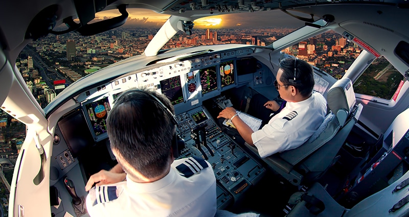 Two pilots flying above city at sunset