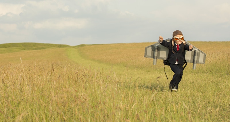 Boy running through field with toy wings