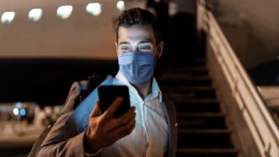 Man wearing face mask checking his phone before boarding plane