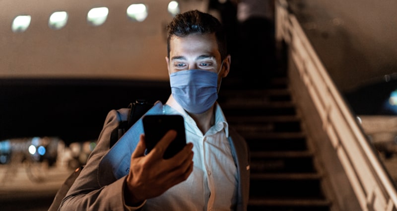 Man wearing face mask checking his phone before boarding plane