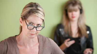 frustrated mom with daughter on cellphone in background